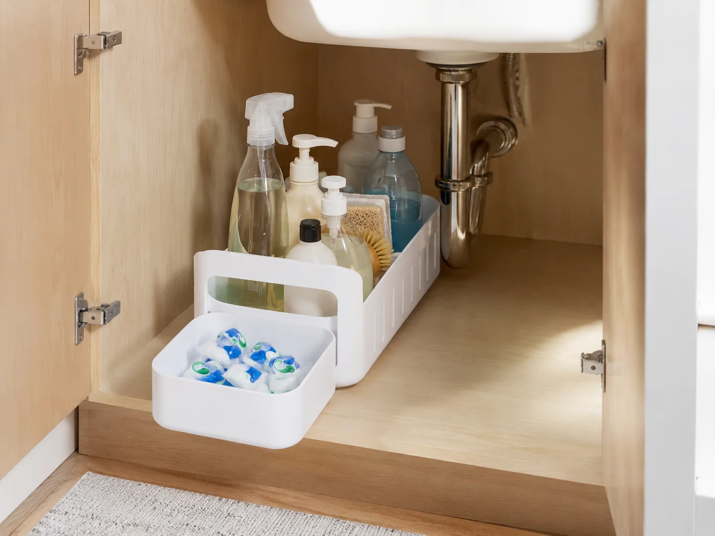 Rolling storage caddy organizing cleaning supplies inside an under-sink kitchen cabinet